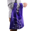 A purple reusable foldaway shopping bag is being held by a person wearing a grey sweater. The bag has a logo.