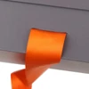 A medium foldable magnetic box in grey with an orange ribbon elegantly emerging from an opening.