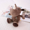 A brown plush rhinoceros toy with a white horn and stitched details, sitting on a textured surface amidst magazines.