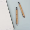 Bamboo pens with stylus nibs in a natural finish, placed beside a blank notebook. One pen features a branding logo.