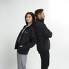 A black unisex soft shell jacket worn by two individuals standing back to back, with one having a logo on the front.