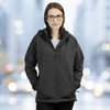 A black soft shell women's jacket with a hood, featuring a logo, worn by a model against a blurred urban background.