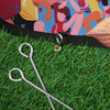 A bean-shaped pop-up banner with a vibrant design and a black edge, accompanied by metallic pegs on grass.
