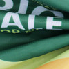 A garden flag featuring green and yellow fabric with a logo. The flag shows part of its designed pattern.