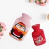 A hot water bottle features a pink penguin knitted cover alongside a red reindeer cover, surrounded by flowers.