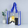 A clear tote bag with blue handles, containing a notebook and a book, displayed next to a small plant.
