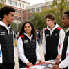 A group of four young people in black puffer jackets with red accents, gathered around a table outdoors.