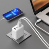 A white 4-port universal travel adapter connected to a power outlet, with a phone and laptop charging.