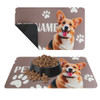 A pet feeding mat featuring a brown background with a corgi's face and paw print designs. It has a logo.