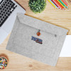 A grey felt laptop bag with a button closure and a logo, placed on a wooden desk alongside stationery and a laptop.