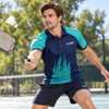 A man wearing a blue and turquoise polo shirt, playing badminton on a court, with a shuttlecock in the air.