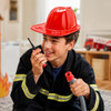 A bright red PVC fire chief hat is worn by a boy holding a walkie-talkie, dressed in a firefighter costume.