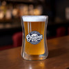 A drink bottle with a double wall glass design, featuring a light amber beverage and a circular logo.