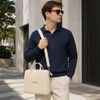 A beige laptop bag with a buffer pad, carried by a man wearing sunglasses, set against a modern urban background.