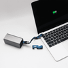 A silver power bank connected to a laptop with a blue charging cable, featuring a phone stand and opener.