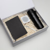 A black drink bottle, notebook, white speaker, and pen in a gift box with shredded paper filling.