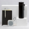 A black drink bottle, a black notebook, a white speaker, and a pen arranged on white pedestals. All products have branding.