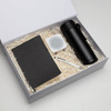 A black notebook, a white speaker, a black drink bottle, and a pen in a gift box with shredded paper.