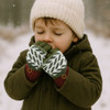 A child wearing green and white jacquard fingerless gloves with a flip cover, and a cream beanie, standing in snow.
