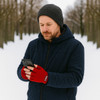 A man in a navy jacket and a grey beanie wears red fingerless gloves while using a smartphone in a snowy lane.