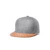 A grey flat cap with a cork brim, featuring a logo on the side.