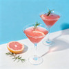 Two classic martini glasses filled with pink grapefruit cocktails, garnished with rosemary, against a blue background.