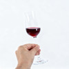 A hand holds a clear glass tulip wine glass containing red wine. The glass features a slender stem and a flared bowl.