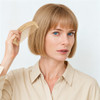 A bamboo small comb held by a person with blonde hair, styled in a bob, wearing a beige shirt.