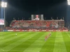 A large polyester TIFO banner in vibrant colours displayed at a stadium, with fans and a field in the foreground.