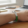 A sleek bracelet featuring a silver clasp and black and green silicone bands, resting on a wooden desk.