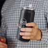 A drink bottle in matte black with a silver lid and a logo on the front, held in a person's hand.