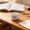 A white ceramic mug with a handle, placed on a wooden table, alongside notebooks and an open book.