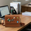 A brown EVA holes briefcase with various decorative pins sits on a desk beside a laptop and stationery.