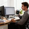 A stainless steel double wall travel mug in black, held by a person sitting at a desk with a computer.