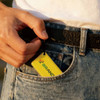 A hand holding a yellow NFC epoxy square tag, with a logo, tucked into the pocket of denim jeans.