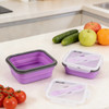 A reusable silicone food storage container in purple, with a white lid, alongside fresh tomatoes, cucumbers, and apples.