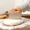 A beechwood handle flour cutter with a metal blade is shown cutting dough on a wooden surface, surrounded by flour.