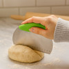 A green flour cutter with measurements held over a ball of dough on a marble countertop.