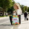 A tote bag in vibrant colours featuring a tropical design with flowers and fruits, alongside a person walking outdoors.