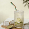 A glass of cocktail with ice, garnished with lime slices, features a green and white striped bendable paper straw.