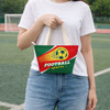 A person holds a green and red tote bag featuring a football design and a logo. The bag has cream handles.