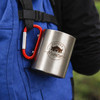 A stainless steel insulated travel mug, silver in colour, attached with a red carabiner handle.
