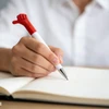 A pen with a red fist-shaped top and a white barrel, held in hand above a notebook.