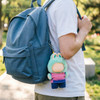 A plush doll in a green and pink outfit attached to a blue backpack, featuring a keychain.