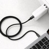 A black braided charging cable connected to a white power adapter and a laptop. It features a logo on the cable.