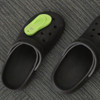 A pair of black clog shoes with a bright green thongs-shaped charm attached to one.