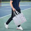 A grey lightweight tennis tote bag with handles, featuring a logo and elastic bungee cord, carried by a person on a tennis court.