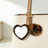 A heart-shaped mirror and a comb keyring in tortoiseshell design, attached to a light-coloured handbag.