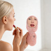 A pink portable acetate hair comb with a mirror, held by a person applying lipstick. The product features a logo.