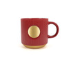 A red ceramic coffee mug featuring a bronze medal design and ribbed texture, with a curved handle.